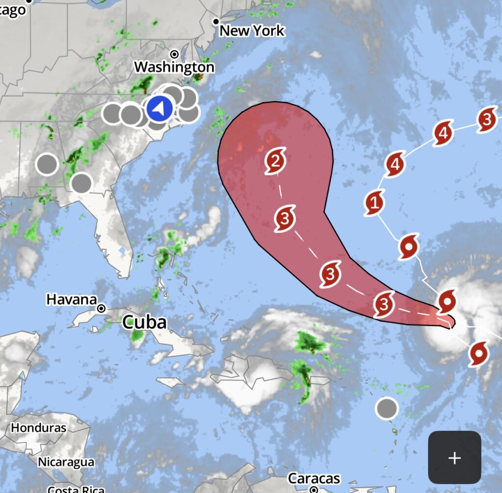 Hurricane forecast map showing a major storm tracking west-northwest across the Atlantic with projected intensification to Category 4 before curving northward off the U.S. East Coast. The forecast cone includes portions of the southeastern U.S. coast near North Carolina.